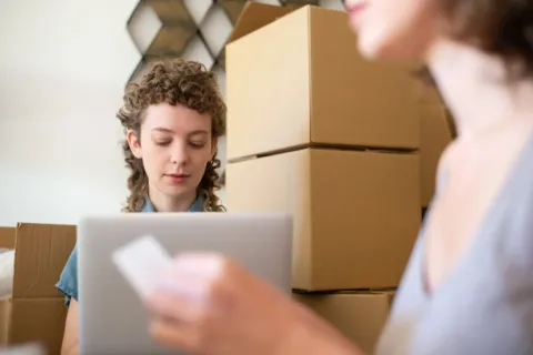 Strategi bisnis reseller online sedang mengemas barang dan memantau pesanan di laptop