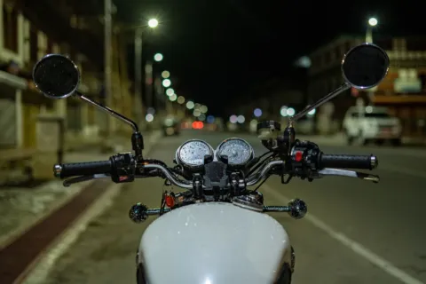 Pengendara mengendarai sepeda motor di jalan raya pada malam hari dengan lampu menyala